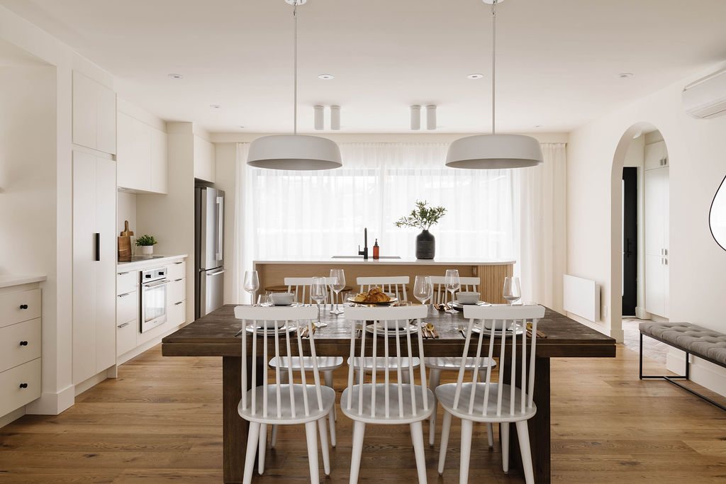 Salle à manger avec table en bois foncé et chaises blanches, cuisine en arrière-plan